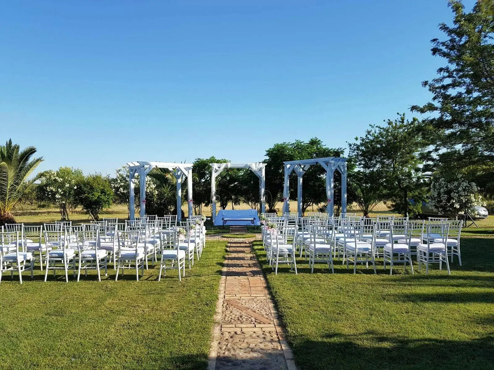 Sillas blancas y pérgolas en el jardín de la ceremonia, con un camino de ladrillo en el centro