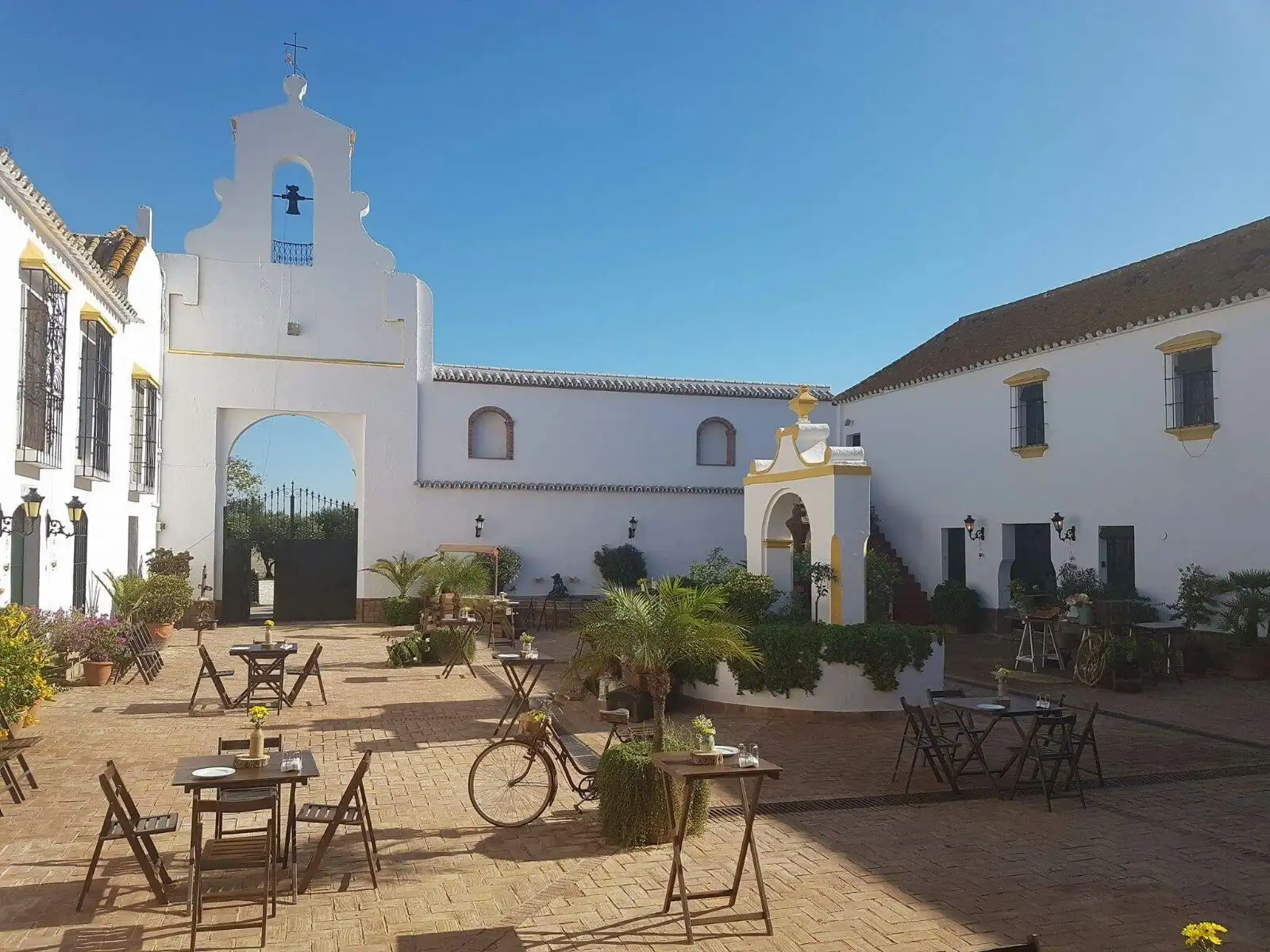 El patio principal bajo la espadaña, con mesas de madera y una bicicleta antigua
